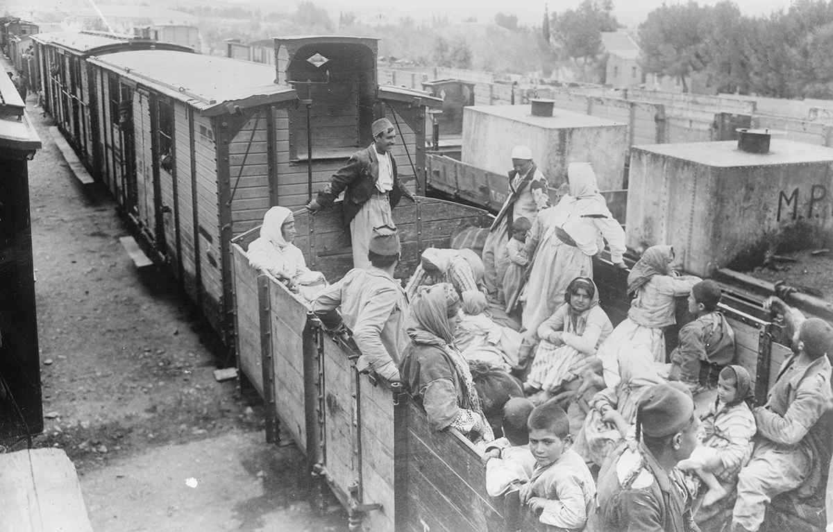 Men, women, and children packed into an uncovered train car, some sitting, some standing.