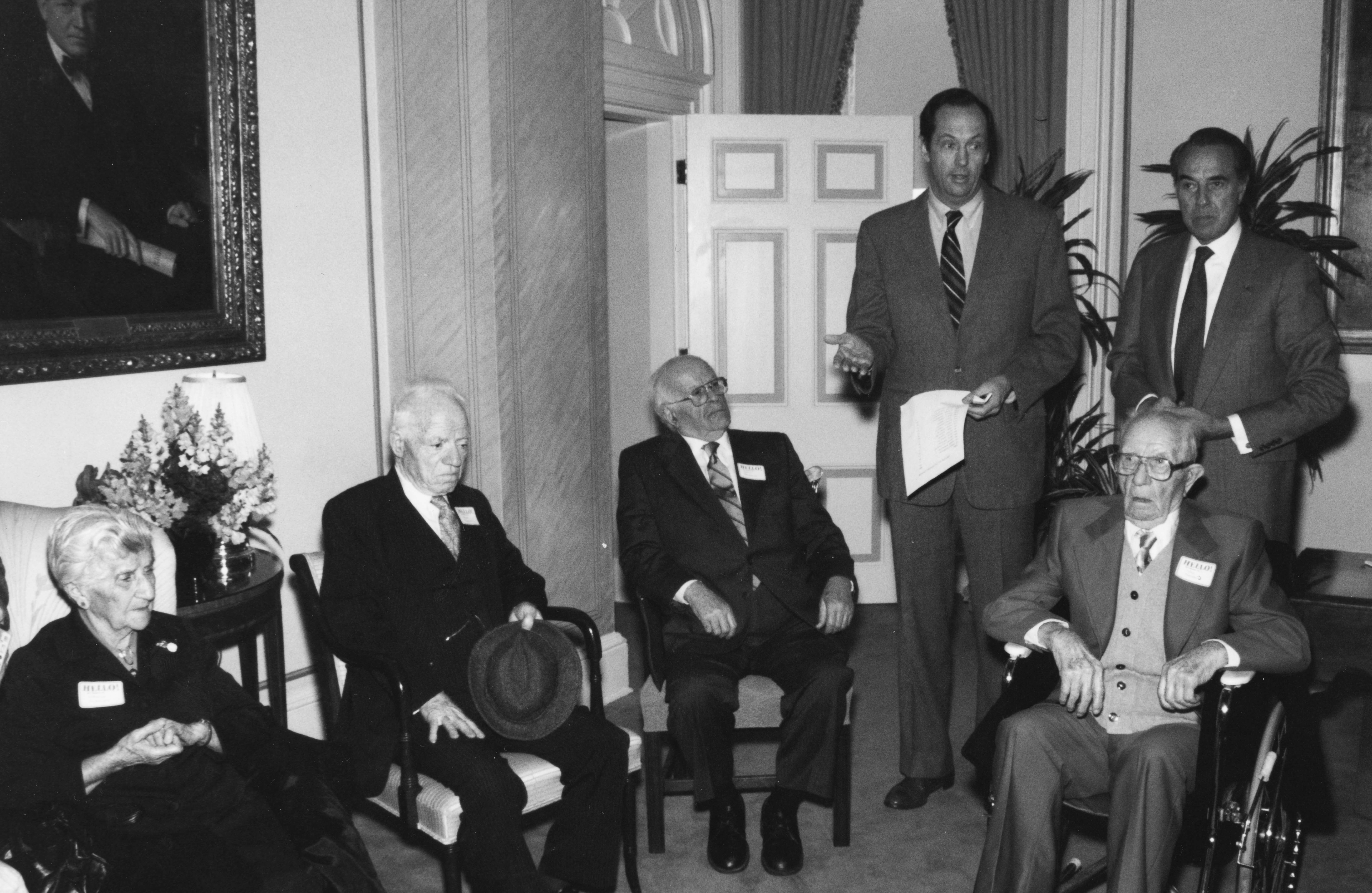 Four well-dressed elderly people seated with two men standing behind.
